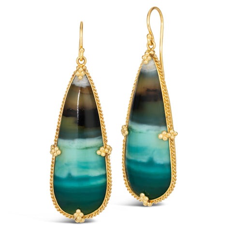 A pair of large teardrop shaped petrified opal earrings are set in an 18k yellow gold chain wrapped bezel with four beaded prongs. The earrings hang on french hook closures.