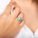 A model wears a round turquoise stone ring set in an 18k yellow gold chain wrapped bezel with four beaded prongs.