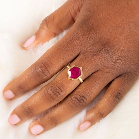 A model wears a hexagon shaped ruby ring with an 18k yellow gold bezel wrapped in a braided chain.