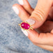 A model holds an oval shaped ruby ring with a braided bezel with four granulated prongs on an 18k yellow gold band.