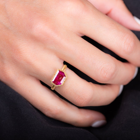A small shield shaped ruby ring is set in an 18k yellow gold chain wrapped bezel and sits on a thin band.