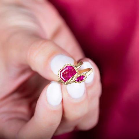 A model holds two small ruby rings set in 18k yellow gold