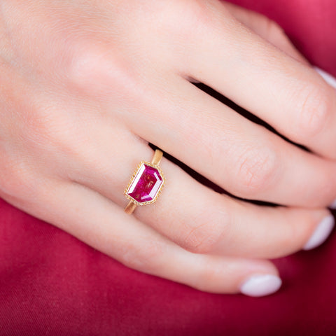 A model wears a small shield shaped ruby ring in an 18k yellow gold chain wrapped bezel.