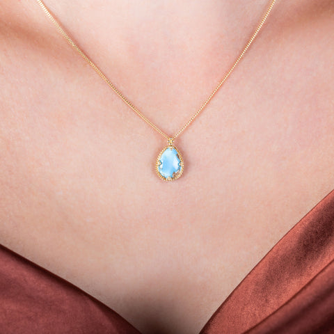 A small teardrop shaped turquoise pendant set in 18k yellow gold hangs from a short chain.