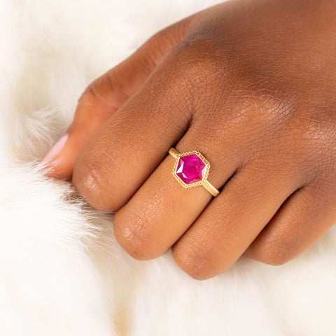 A model wears a small hexagon shaped faceted ruby ring set in 18k yellow gold.