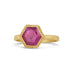 A small faceted ruby shaped like a hexagon is set in an 18k yellow gold bezel with a braided detail around the edge on a thin band