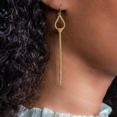 A model wears a long 18k yellow gold teardrop shaped hoop with several chains hanging from the bodies.