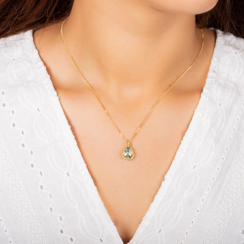 A small teardrop shaped grey diamond pendant is set in an 18k yellow gold chain wrapped bezel with four beaded prongs. The pendant hangs on a delicate short chain.