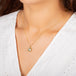 A model wears a small teardrop shaped grey diamond pendant is set in an 18k yellow gold chain wrapped bezel with four beaded prongs. The pendant hangs on a delicate short chain.