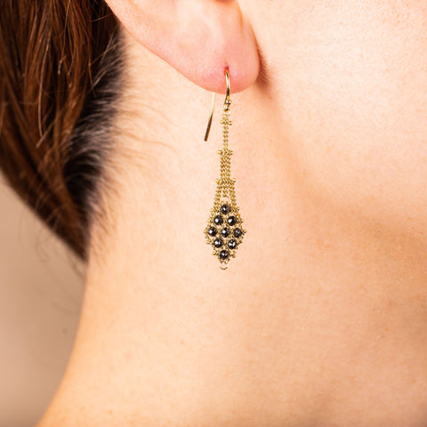 A model wears an earring crafted in 18k yellow gold chain and black diamonds that are woven into a diamond lattice pattern.