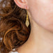 A model wears an earring crafted in 18k yellow gold chain and white pearls that are woven into a diamond lattice pattern.