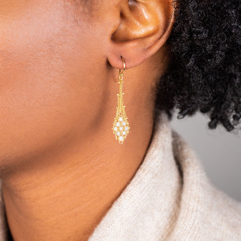 A model wears an earring crafted in 18k yellow gold chain and silver diamonds that are woven into a diamond lattice pattern.