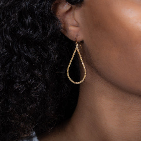 A model wears a large teardrop shaped 18k yellow gold earring with a stardust-like finish.