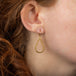 A model wears a small teardrop shaped 18k yellow gold earring with a stardust-like finish.