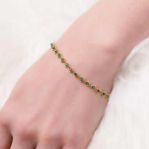 A model wears a delicate woven 18k yellow gold chain bracelet with blue diamonds. 