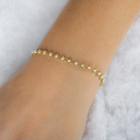 This 18k yellow gold bracelet features white pearl beads woven throughout a delicate chain. The bracelet features a lobster clasp closure.