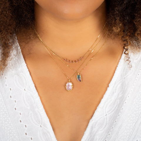 A model wears a stack of three necklaces, including a morganite pendant, a watermelon tourmaline pendant, and a ruby chain. 