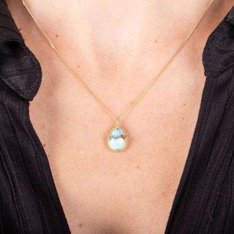 A small teardrop shaped turquoise pendant is set in 18k yellow gold and hangs on a short chain.