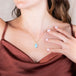 A model wears a teardrop shaped turquoise pendant that is wrapped in 18k yellow gold and hangs on a delicate gold chain.