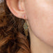 A model wears an 18k yellow gold earring crafted with blue diamonds woven into a diamond shaped lattice pattern and has three dangling chains at the bottom.