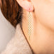 A pair of long white pearl earrings features a woven lattice pattern and two dangling chains at the bottom of the earring. The earrings fasten with french hook closures.