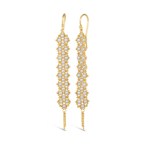 A pair of long white pearl earrings features a woven lattice pattern and two dangling chains at the bottom of the earring. The earrings fasten with french hook closures.